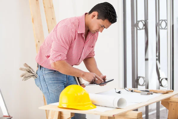 Engenheiro hispânico atraente revisando um plano de piso em um computador tablet — Fotografia de Stock