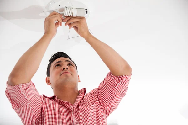 Young Hispanic man replacing some light bulbs from a lamp on the ceiling — Stock Photo, Image