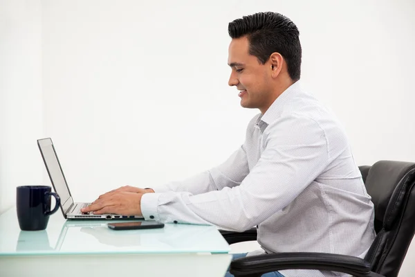 Glücklicher junger Mann Social Networking auf seinem Laptop im Büro — Stockfoto