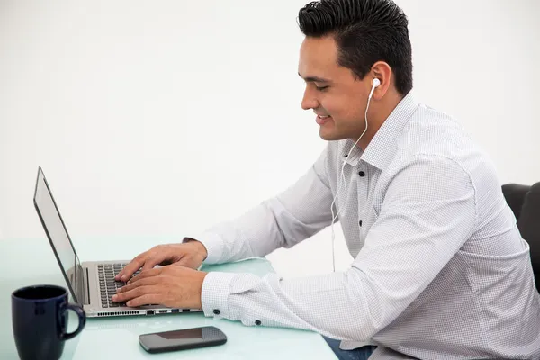 Jonge Spaanse man oordopjes dragen tijdens het werken aan zijn laptop op het kantoor — Stockfoto