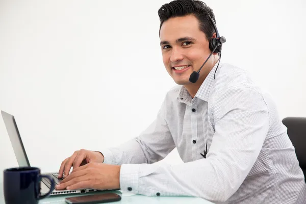 Bonito hispânico vestindo um fone de ouvido e recebendo uma chamada de um cliente no trabalho — Fotografia de Stock