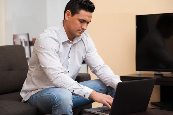 Jovem latino trabalhando em casa usando um computador portátil na sala de estar — Fotografia de Stock