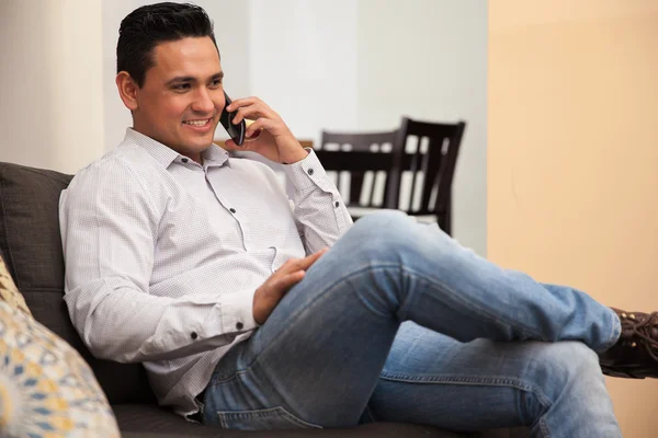 Handsome Hispanik pemuda berbicara di telepon genggamnya sambil bersantai di rumah — Stok Foto