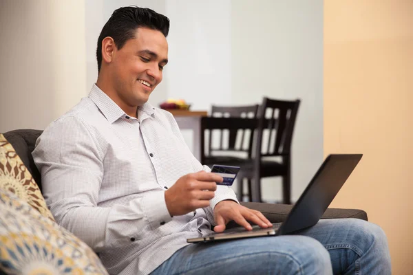 Attrayant homme hispanique en utilisant sa carte de crédit et ordinateur portable pour réserver un voyage en ligne — Photo