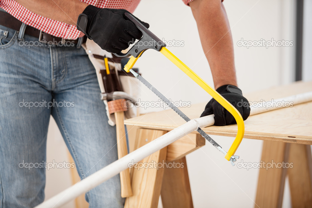 Closeup of a plumber using a hacksaw to cut down some pipes