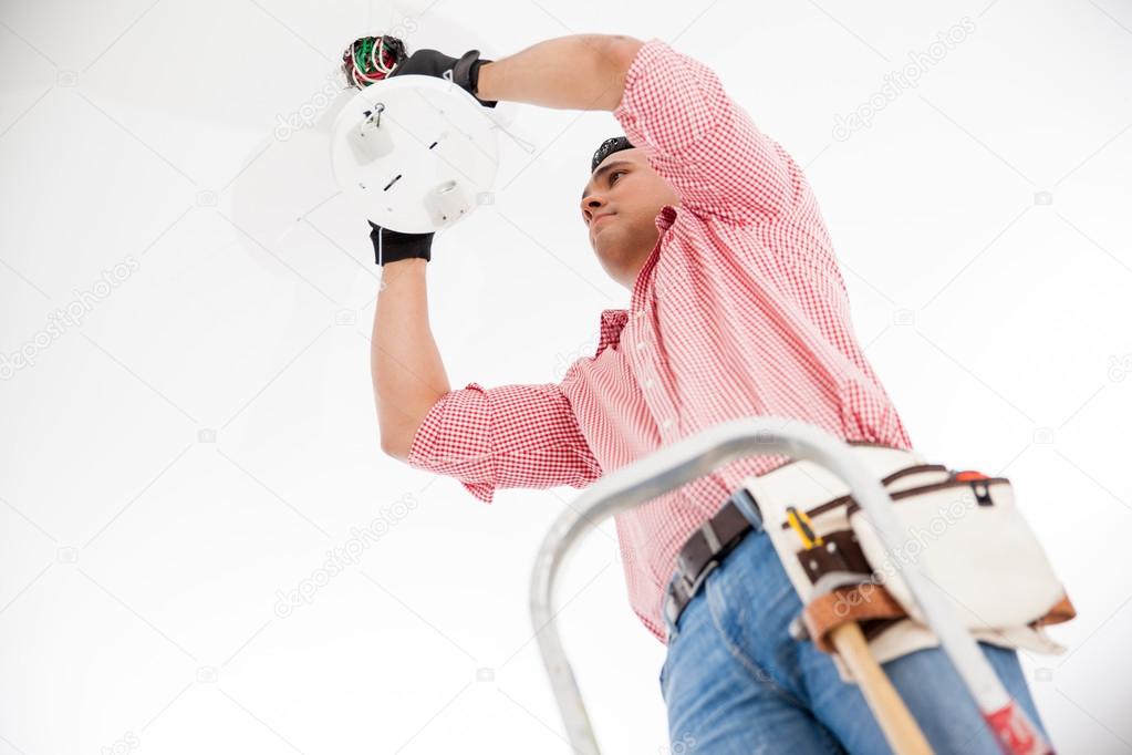 Young Hispanic electrician wiring a lamp fixture on the ceiling