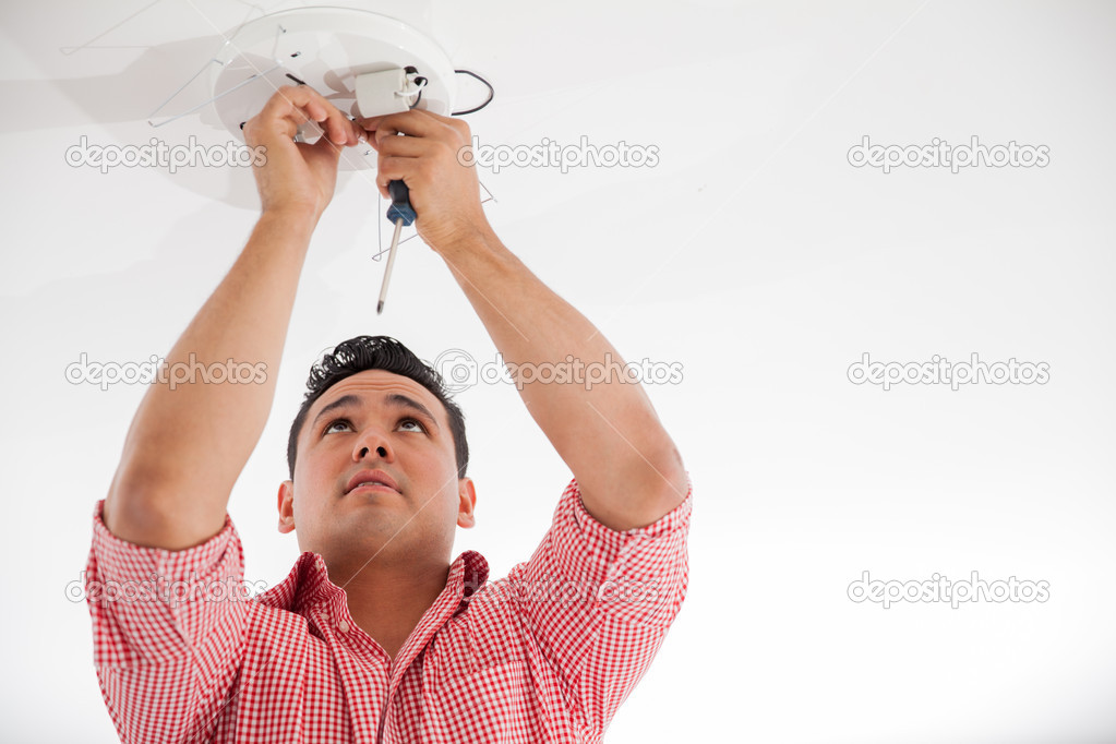 Handsome young man using a screwdriver to install a lamp on the ceiling