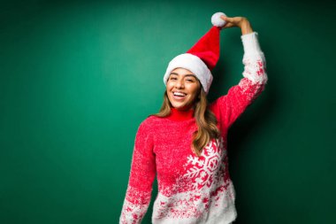 Noel Baba şapkası takan ve Noel 'de stüdyonun yeşil arka planında eğlenen oyuncu kadın.