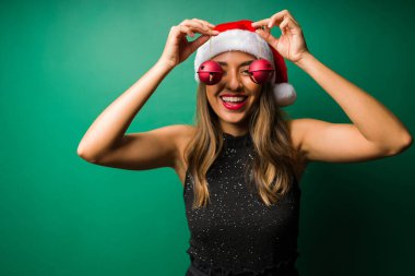 Eğlenceli genç bir kadın Noel süsleriyle oynuyor ve yeşil bir arka plana gülüyor.