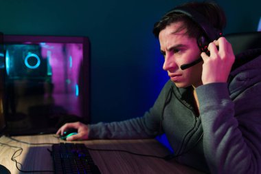 Genç adam bilgisayar ekranına bakıp video oyunları oynarken kulaklıkla rakibiyle konuşuyor.