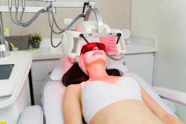 Güzeller güzeli bir kadın güzellik kliniğinde yüz bakımı ve LED maske yaptırıyor.
