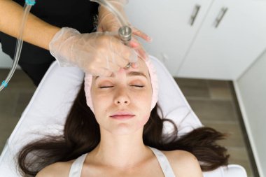 Gözleri kapalı, rahat genç bir kadın, pürüzsüz bir cilt için mikro cilt bakımı yaptırıyor.