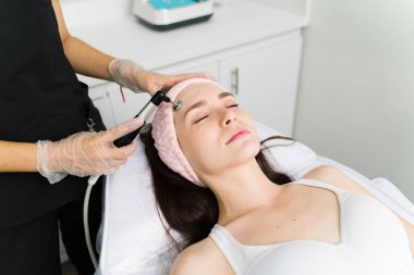 Güzel bir genç kadın, profesyonel bir güzellik uzmanıyla pürüzsüz ve parlak bir cilde sahip olmak için yaşlanma karşıtı bir tedavi uyguluyor.