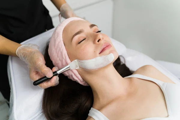 Beautician applying exfoliating cream on the skin face of a female customer at the beauty parlor