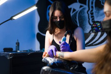 Dövme salonunda kadın müşteriye dövme yaptıran profesyonel sanatçı genç bir kadın.