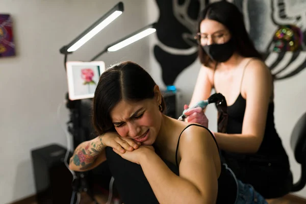 It hurts a lot. Stressed young woman getting a back tattoo at the ink studio with a professional female tattoo artist