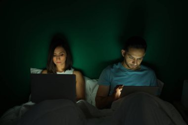 Latin kökenli güzel bir çift gece boyunca laptoplarıyla yataklarında çalışıyor. 