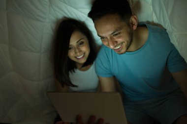 Sıcak bir gecede yorganın altında dinlenen heyecanlı çift yatakta bir tablette film ya da video izliyor. 