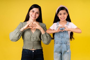 Aile sevgisi her şeydir. Neşeli genç bir kadın ve küçük bir kız sarı bir arka plana karşı kalp hareketi yapıyorlar.