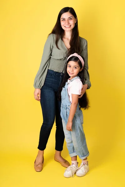 美しいです若いですお母さんと女の子抱擁と見てカメラに対してA黄色の背景 — ストック写真