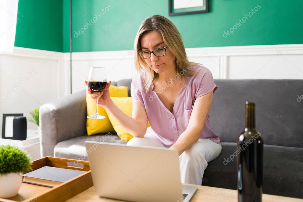 Caucasian mature woman typing on the laptop and doing online shopping while drinking wine 