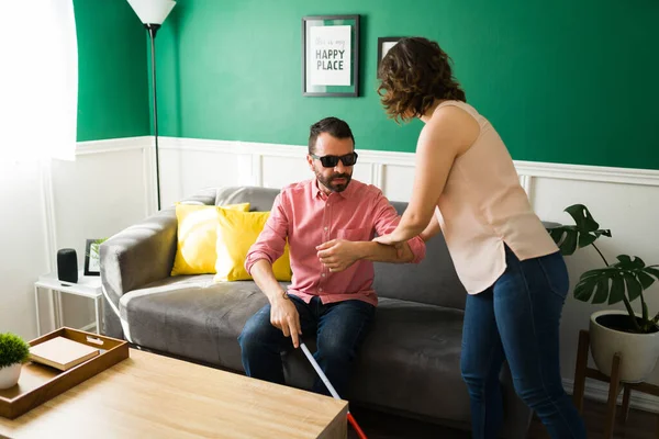 Caring woman and friend helping a blind latin man with a walking stick to get out of the house