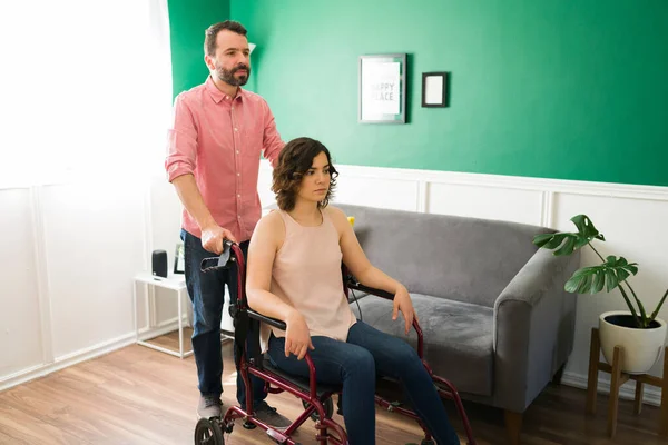 可爱的男朋友推着她的女朋友的轮椅 一个年轻人帮助一个瘫痪的女人在房子里走动 — 图库照片