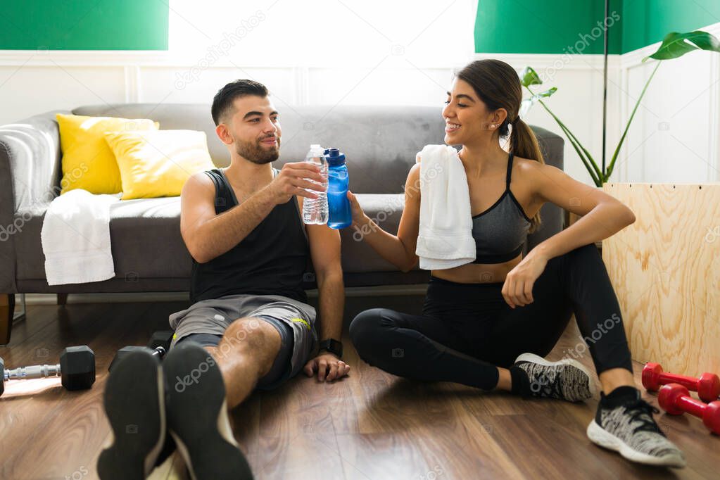 Attractive young man and woman drinking water after doing their cardio workout in the living room