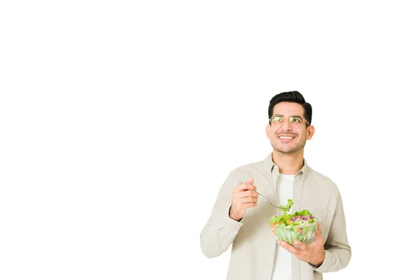 一个沉默寡言的年轻人一边想着食物 一边微笑着吃着美味的绿色沙拉 — 图库照片