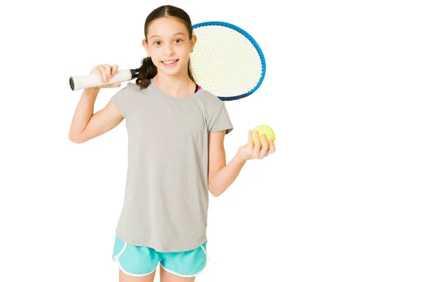 明るいですPreteen女の子でアクティブな身に着けていますホワイト背景に笑顔ながらテニスボールとラケット — ストック写真