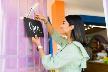 Resmi olarak açığız. Neşeli işyeri sahibi moda giyim mağazasının kapısına açık tabela asıyor. 