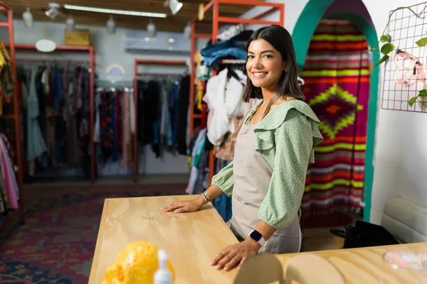 I\'m ready for the customers. Happy latin woman at the cashier while working at a thrift or clothing store
