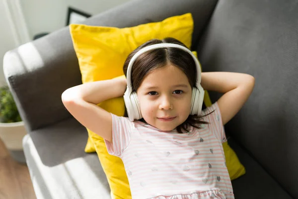 可爱的小女孩一边用无线耳机听音乐一边放松 可爱的孩子躺在沙发上 — 图库照片