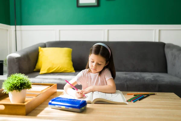 リビングルームで一人で宿題をしている素直な女の子 ぬり絵で遊ぶ小学生 — ストック写真