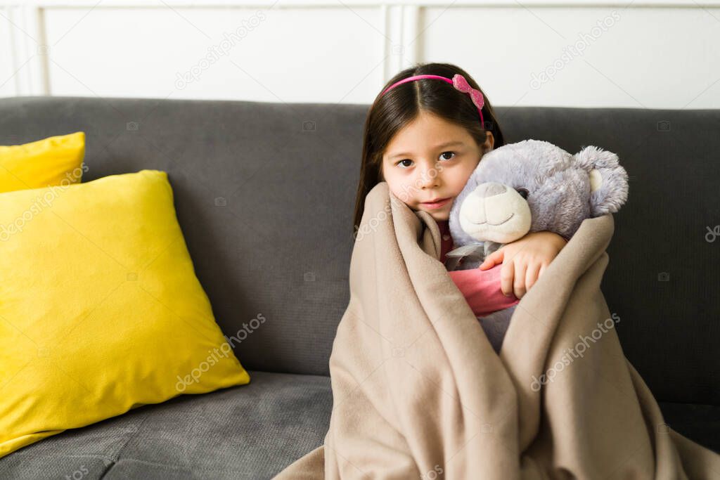 It's so chilly outside. Beautiful child hugging her teddy bear and feeling cozy under a blanket while relaxing during winter 