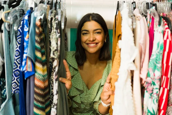 Attractive hispanic woman standing between racks of clothes at the trendy apparel boutique