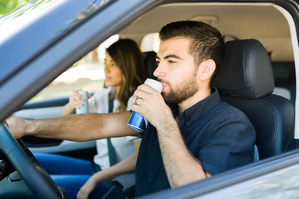喉の渇き若い男が酒を飲んで一緒に旅行中にガールフレンドと車を運転する — ストック写真