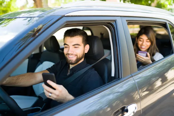 スマートフォンでライドシェアアプリを見ている間にハンサムな男性ドライバーと女性の乗客笑顔 — ストック写真