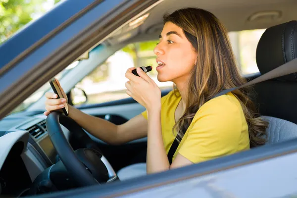 朝働くために彼女の車を運転しながら口紅を身に着けている豪華なヒスパニック系女性の側面図 — ストック写真