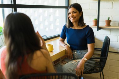 Çekici İspanyol kadın kahkahalarla gülüyor ve kahve dükkanında en iyi arkadaşıyla harika vakit geçiriyor. 