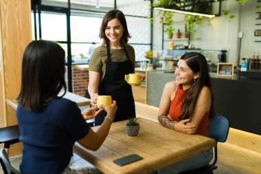 Siparişiniz hazır. Neşeli garson bir grup arkadaş için masaya kahve getiriyor.