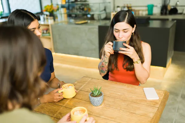 コーヒーショップで親友と話している間に美しい若い女性がおいしいラテを飲んでいます — ストック写真