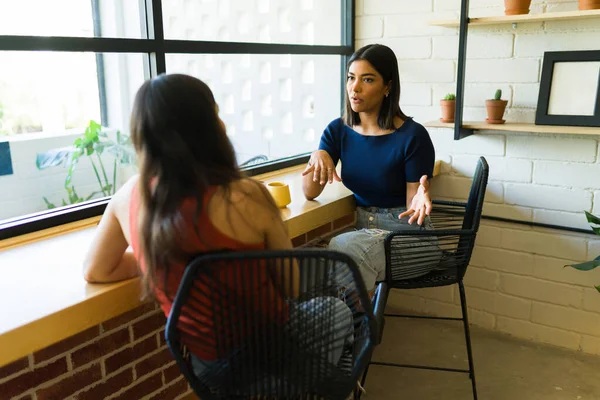 ラテン系の若い女性がコーヒーを飲みながらカフェで友人と話して追いつく — ストック写真