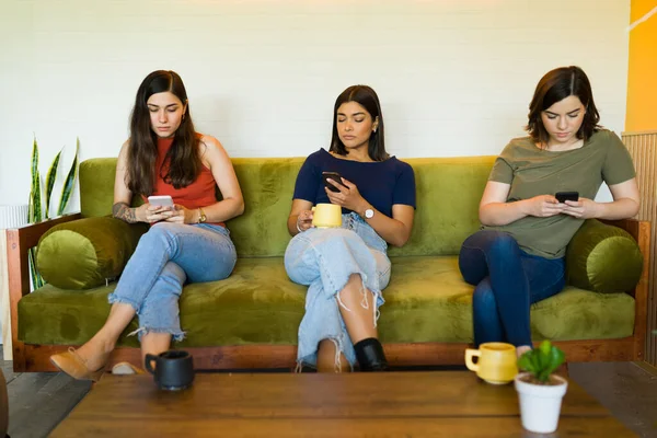 コーヒーショップのソファに座りながら 女性の友達がスマホでテキストメッセージやSnsを利用している — ストック写真
