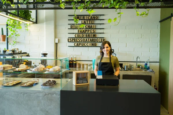 Kasiyerdeki neşeli çekici iş sahibi kahve dükkanındaki müşterilerle ilgilenmek için tablet kullanıyor.
