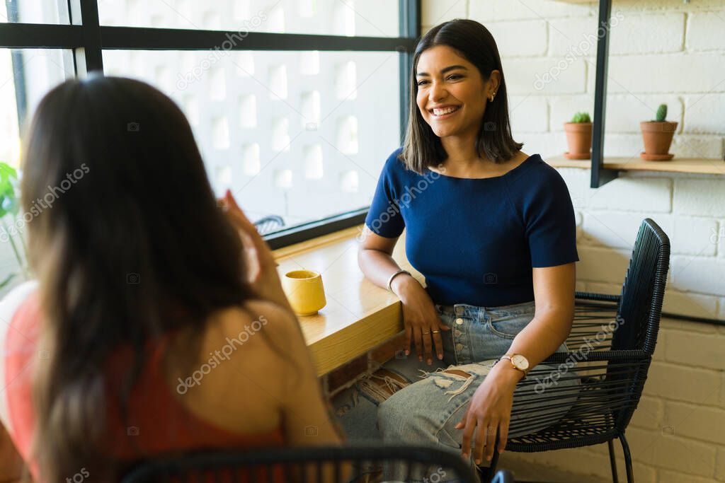 Attractive hispanic woman laughing and having a great time at the coffee shop with her best friend 