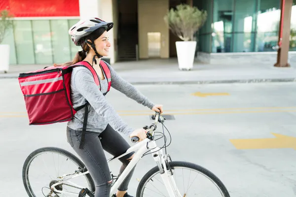 街中で食べ物を配達しながら 自転車に乗って笑顔で赤いバックパックを持つ美しい幸せな配達の女の子 — ストック写真