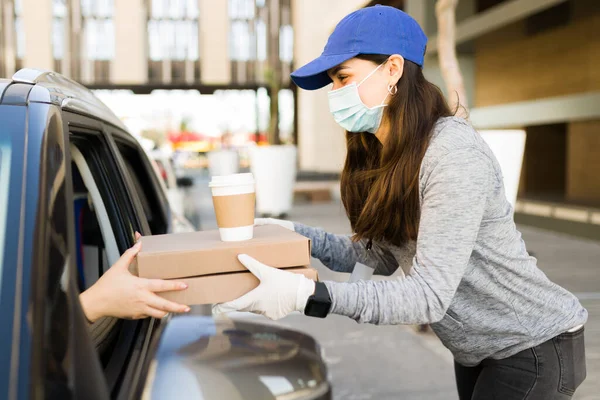 パンデミック時に食料を供給する 車の中で顧客にピザの注文を与える顔のマスクを持つ若い女性 — ストック写真