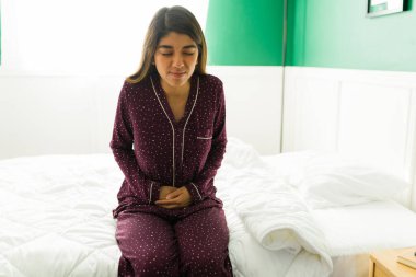 Kötü bir mide ağrısı çeken ve sabah uyandıktan sonra kendini hasta hisseden pijamalı acı çeken genç bir kadın.