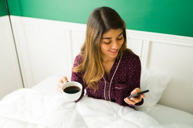 Göz kamaştırıcı İspanyol bir kadının yatakta bir fincan kahve içip mesajlaşmasının yüksek açılı görüntüsü. 